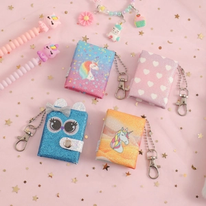 Flat lay of colorful glitter mini notebooks with unicorn and owl patterns on pink sequins