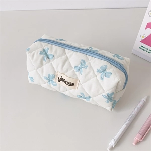 Quilted cream pencil case with blue bow print and branded patch on a desk