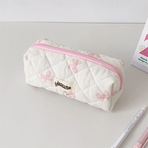 Detail of white quilted pencil case with pink bows and brand label on a desk