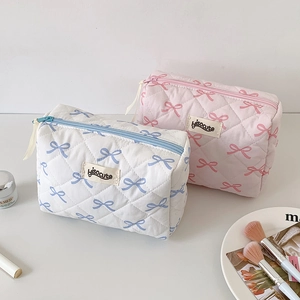 Quilted bow-print cosmetic bags in pink and blue displayed with makeup accessories