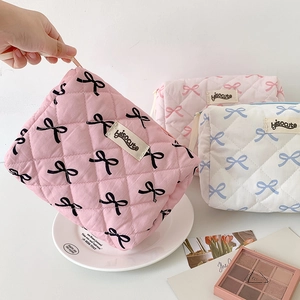 Soft quilted bow makeup bags in pink and white shown in a portable handheld lifestyle view