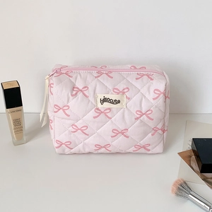 Pink quilted makeup bag with bow print and brand tag displayed with cosmetics