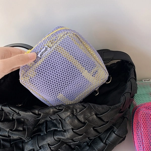 Detail of hand placing the purple mesh pouch with yellow zipper into a larger tote bag