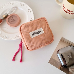 Detailed shot of quilted orange checkered small makeup pouch with branded woven label