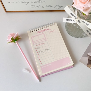 Flat lay of pink rose ballpoint pen and spiral notebook with daily planner pages
