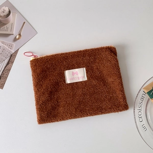 Close-up of brown plush cosmetic bag with pink bow logo and soft fuzzy texture details