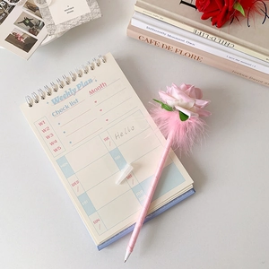 Primer plano de bolígrafo de rosa rosa con cuaderno de plan semanal en escritorio suave