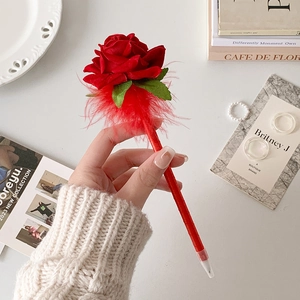 Detalle de bolígrafo con rosa de seda roja y plumas con cinta envuelta sostenido a mano