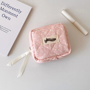 Detailed view of pink quilted mini storage pouch with ribbon zipper pulls and woven logo tag