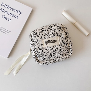 Close-up of quilted makeup bag featuring ink splatter pattern and white ribbon zipper pull