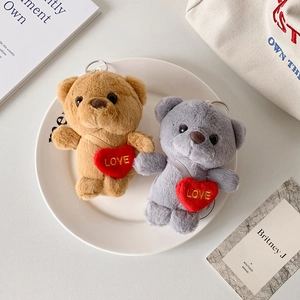 Macro detail of plush teddy bear keychains with LOVE heart embroidery on white plate