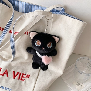 Cute black plush cat keychain with pink heart decoration hanging on a white canvas bag