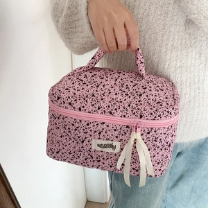 Pink quilted makeup bag with black ink splatter pattern and convenient top carry handle