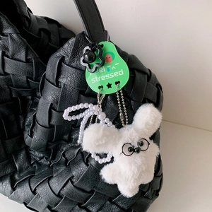 Close-up of white plush fruit keychain with glasses and green tag on black bag
