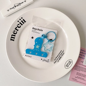 Detail of blue acrylic star keychain and hairclip pendant on branding card in a white tray
