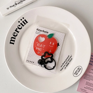 Detail of red apple acrylic keychain with Eat Me text on a decorative white plate