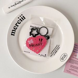 Close-up of pink acrylic heart keychain with black star ring and decorative packaging