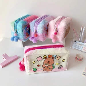 Flat lay of colorful plush pencil cases with cute bear patterns and fluffy pompom charms