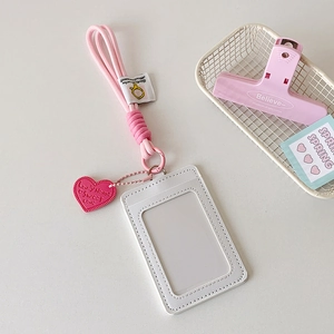 Vertical white ID card holder with pink braided lanyard and heart pendant on white desk