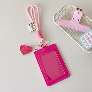 Pink PU leather ID card holder with woven lanyard and heart charm on white desk