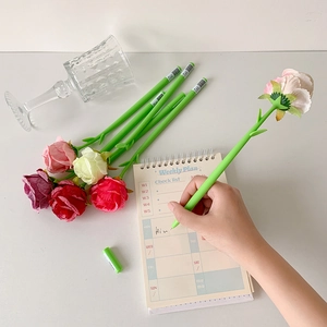 Creative rose-shaped ballpoint pen held in hand writing on a minimalist white desk setup