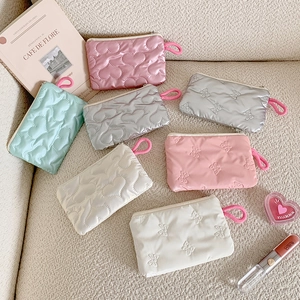Quilted heart and bow makeup bags in silver, pink, and mint displayed on a sofa