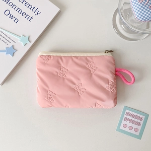 Macro detail of pink cosmetic bag with 3D bow texture, zipper, and wrist strap