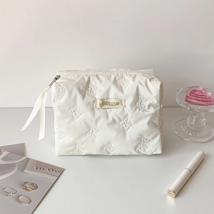 Detail of white quilted cosmetic bag featuring butterfly embossing and ribbon zipper pull