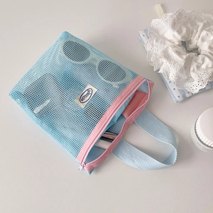 Macro detail of blue mesh storage bag with pink zipper holding sunglasses and skincare
