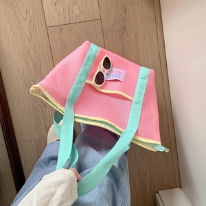 Detalle de bolso de malla rosa con asas verdes y etiqueta THE BEST MOMENT en suelo madera
