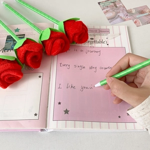 Red 3D rose ballpoint pen with green stem held in hand writing on a pink notebook