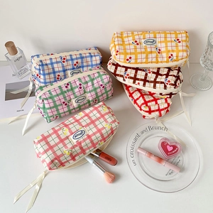 Detail showing checkered canvas pencil cases with cherry prints and white ribbon zippers
