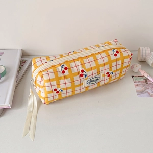 Detail of yellow plaid pencil case with cherry print, ribbon zipper, and brand label