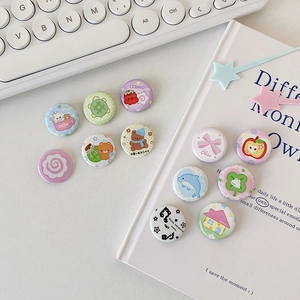 Flat lay of 11 cute cartoon tinplate badges on a white keyboard and book background