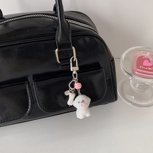 Porte-clés chien bichon en peluche blanche avec breloque os sur un sac à main noir