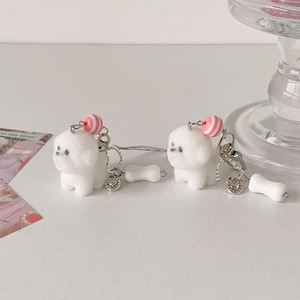 Détail de breloques chiot en peluche blanche avec accessoires os et médailles cœur