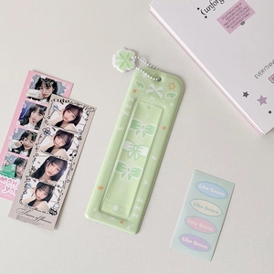 Close-up of light green photocard holder with bow pendant and chain on a desk