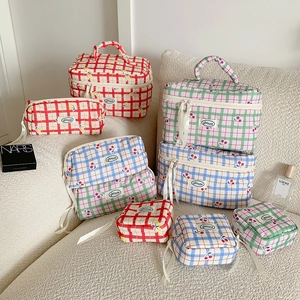 Set di tre pochette per trucchi a quadretti con ciliegie su divano in velluto bianco