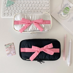 Detailed top view of silver and black bow pencil cases on a minimalist white desk setup