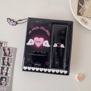 Macro detail of black Y2K photocard album with pink angel text and butterfly wing pendant