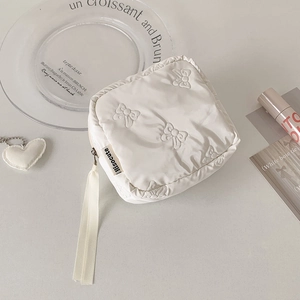 Detail of a quilted cream square pouch with bow texture and a plush heart keychain