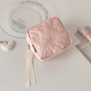 Close-up of pink quilted makeup bag with 3D bow patterns and white ribbon zipper pull