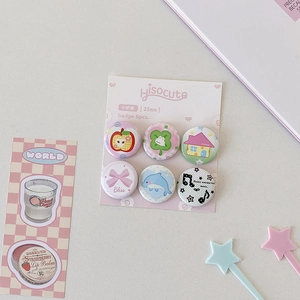 Close-up of 6pc 25mm cartoon tinplate badges with apple and clover icons on pink card
