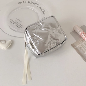 Detail of silver quilted pouch with bow texture and white ribbon zipper pull