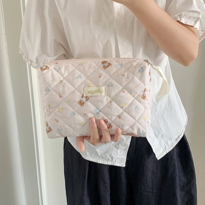 Quilted pink makeup bag with cartoon bear print and floral patterns held by hand