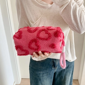 Close-up of soft pink plush cosmetic bag with vibrant heart patterns and hand strap