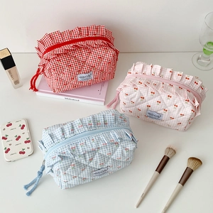 Three quilted cherry and plaid pouches with ruffled zipper edges on a white desk