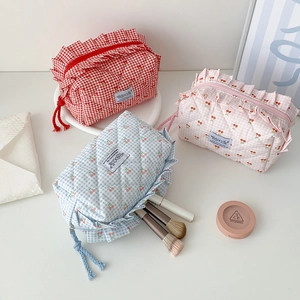 Three cherry quilted pouches in red, pink and blue with ruffled edges on a white table