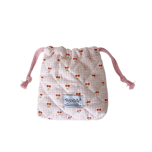 Pink quilted drawstring makeup bag with red cherry prints and cotton texture on white background