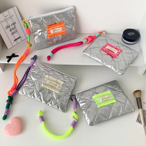 Détail de la trousse de maquillage argentée matelassée avec lanières tissées colorées
